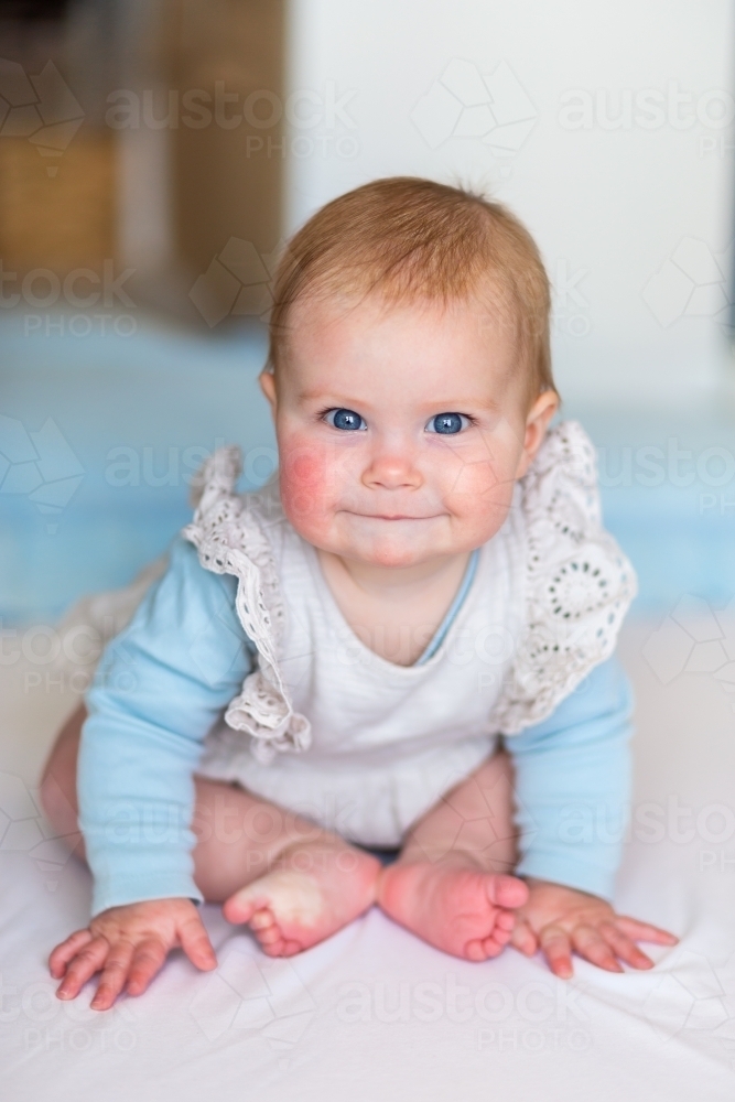 Happy 6 month old baby with a cheeky smile sitting up - Australian Stock Image