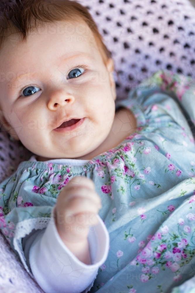 happy 9 week old baby with wide eyes looking up sitting in bouncer on soft pastel crocheted blanket - Australian Stock Image