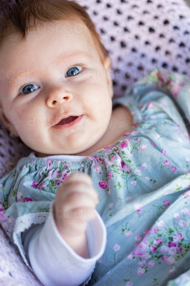 happy 9 week old baby with wide eyes looking at camera sitting in bouncer on crocheted blanket - Australian Stock Image