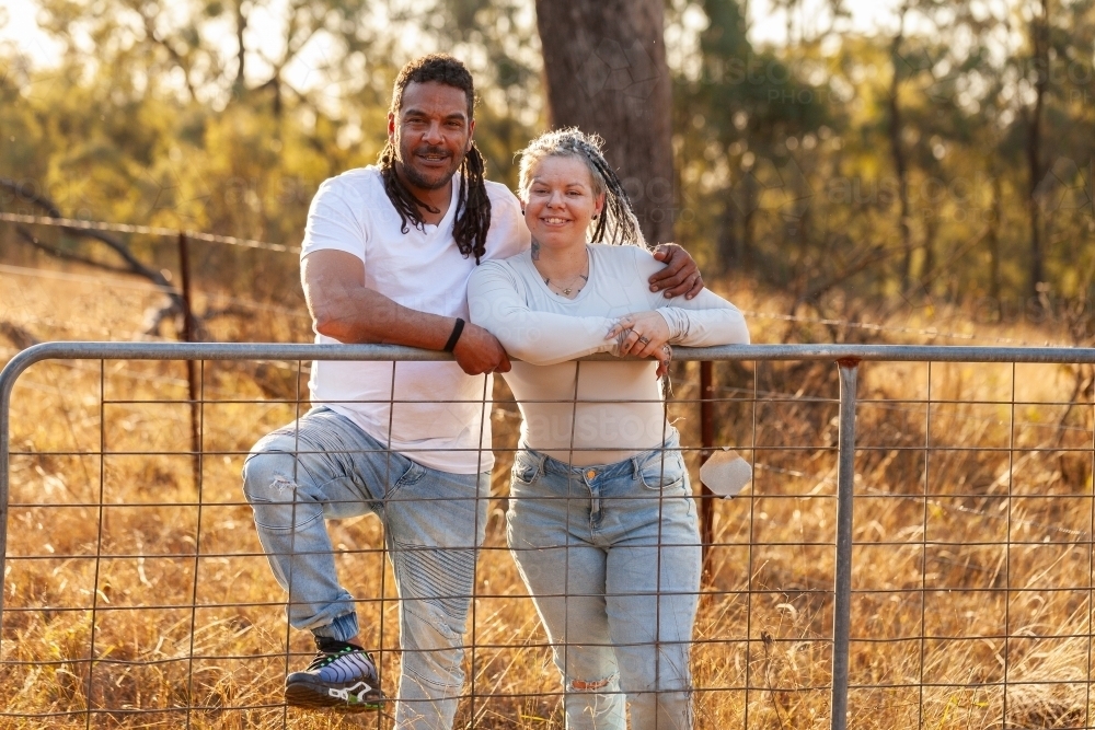 Happy aboriginal Australian couple leaning on farm gate together in country - Australian Stock Image