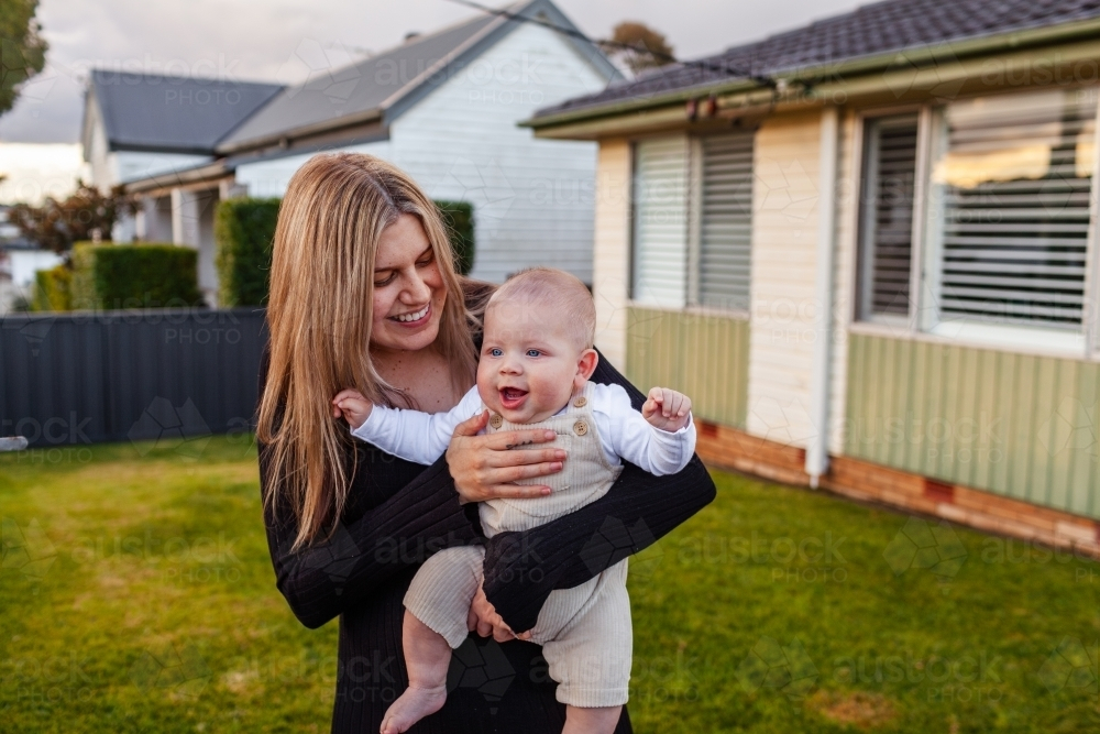 Happy aboriginal australian mother holding her baby boy in front yard of home - Australian Stock Image