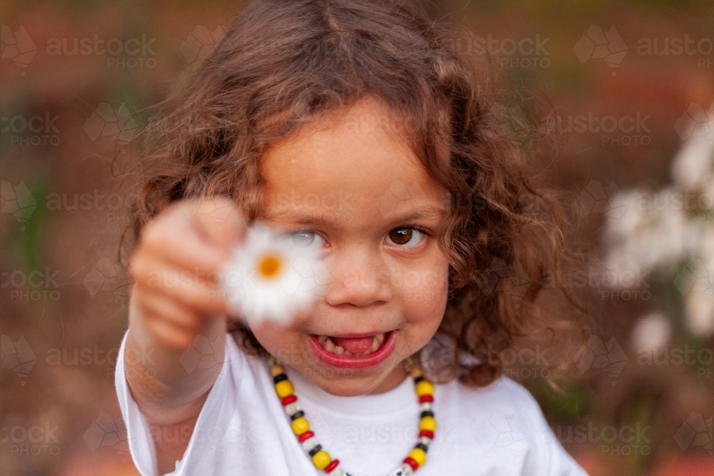 Happy aboriginal girl holding out daisy - Australian Stock Image