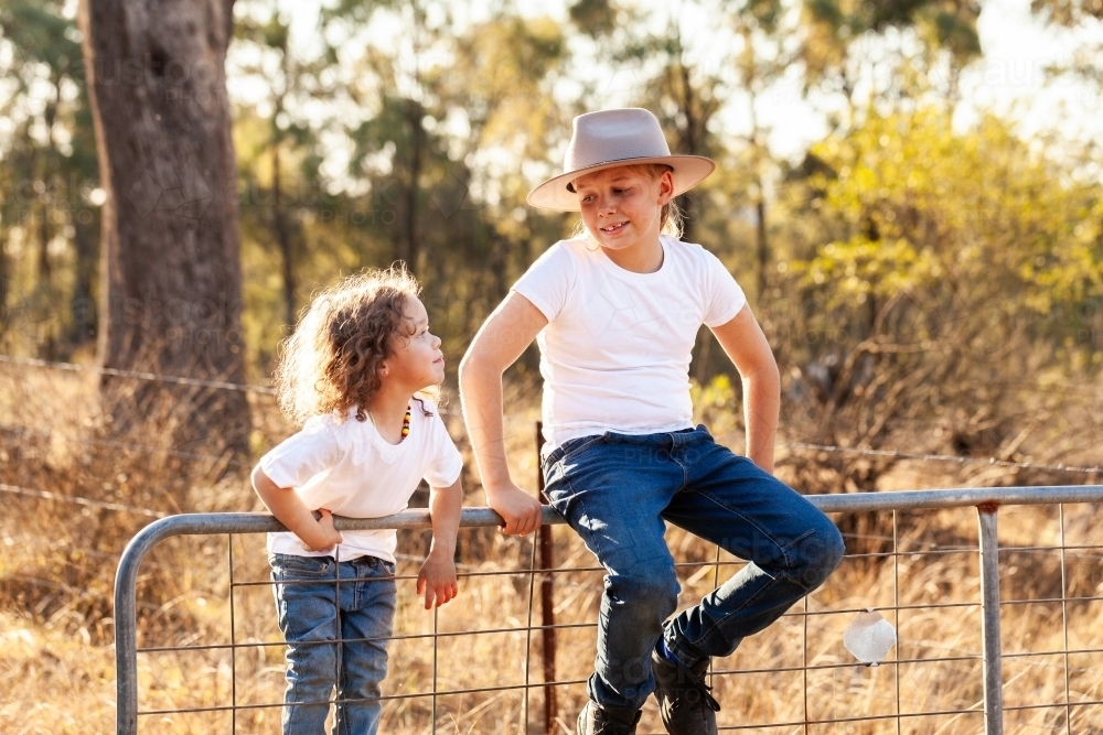 Happy aboriginal kids climbing on fence in farm paddock - Australian Stock Image