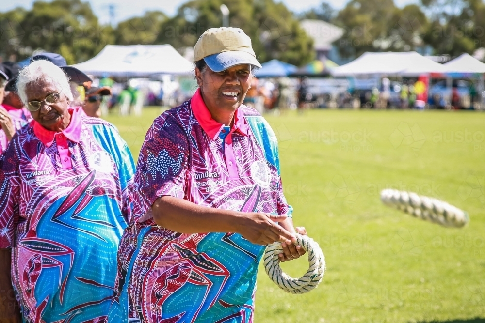 Happy Aboriginal woman smiling wearing hat throwing rope ring quoits - Australian Stock Image