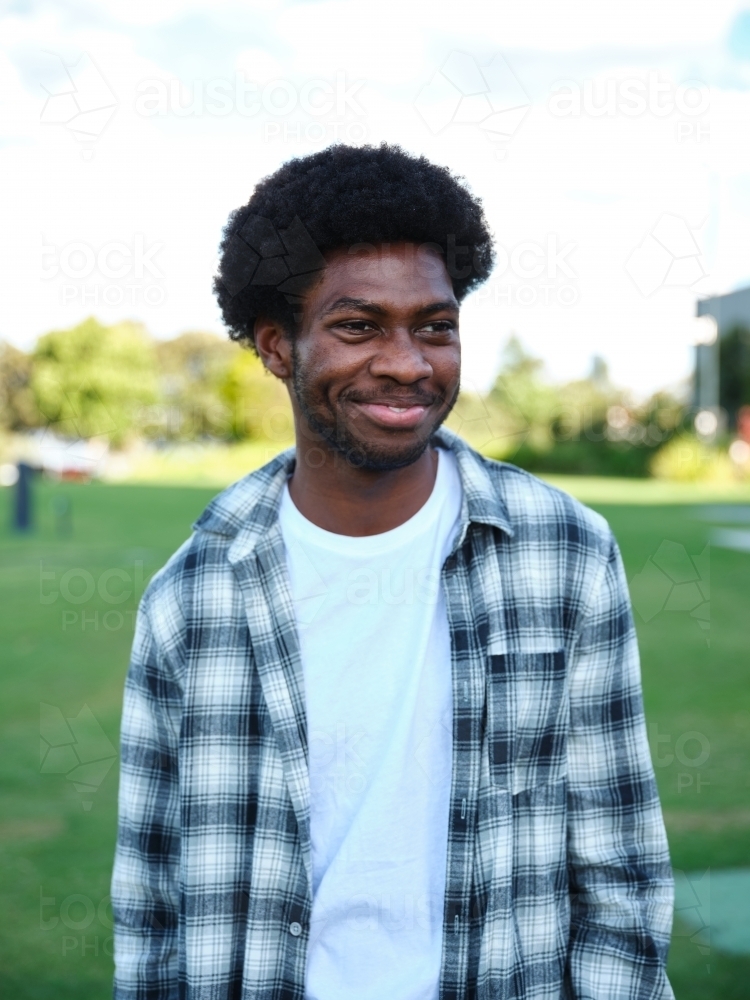 Happy African American man in a park wearing a checkered polo shirt - Australian Stock Image
