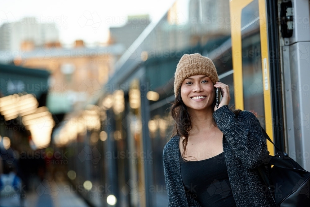 Happy Asian woman getting off train talking on mobile phone - Australian Stock Image