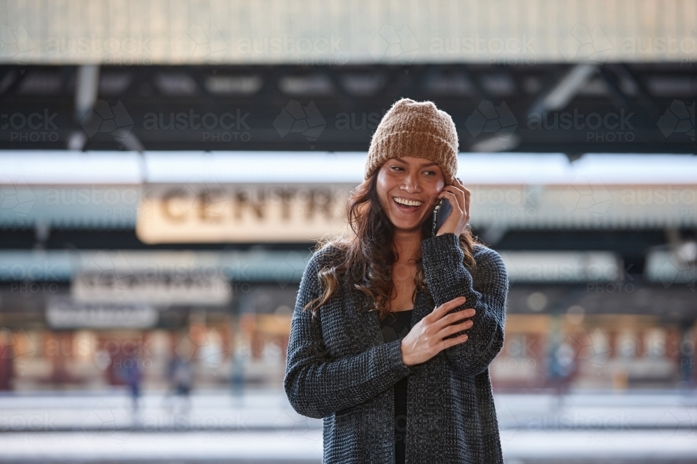 Happy Asian woman talking on mobile whilst waiting at train station - Australian Stock Image