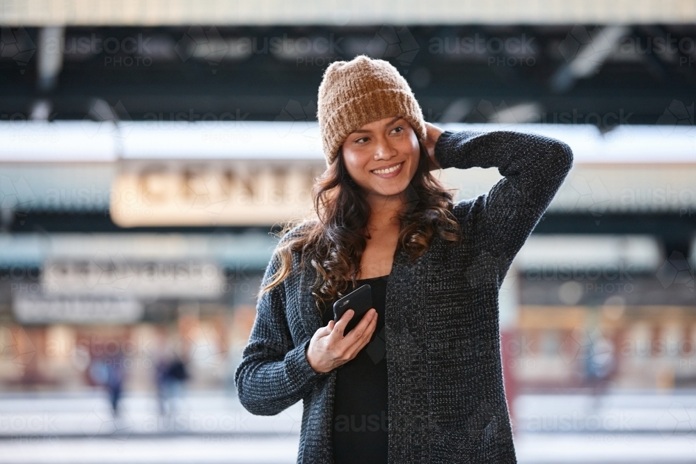 Happy Asian woman waiting at train station with mobile phone - Australian Stock Image
