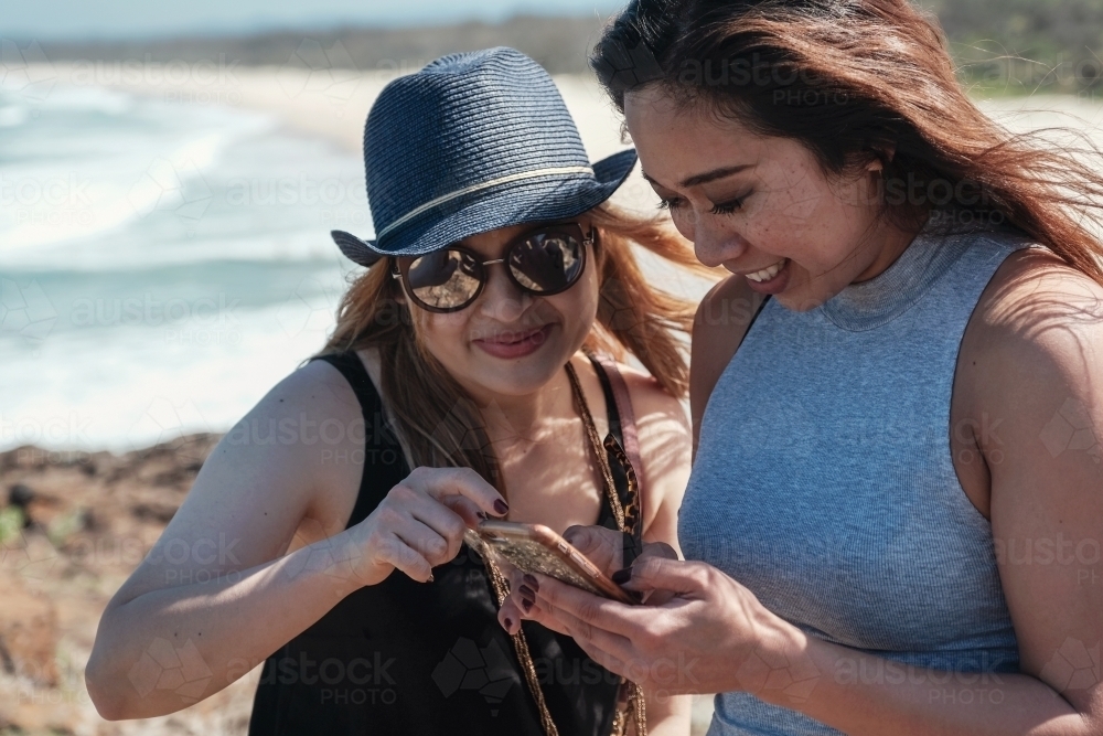 Happy Asian young adult women using smartphone on holidays - Australian Stock Image