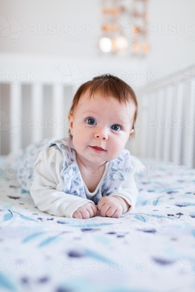 Happy Aussie baby smiling at tummy time in cot in bedroom - Australian Stock Image