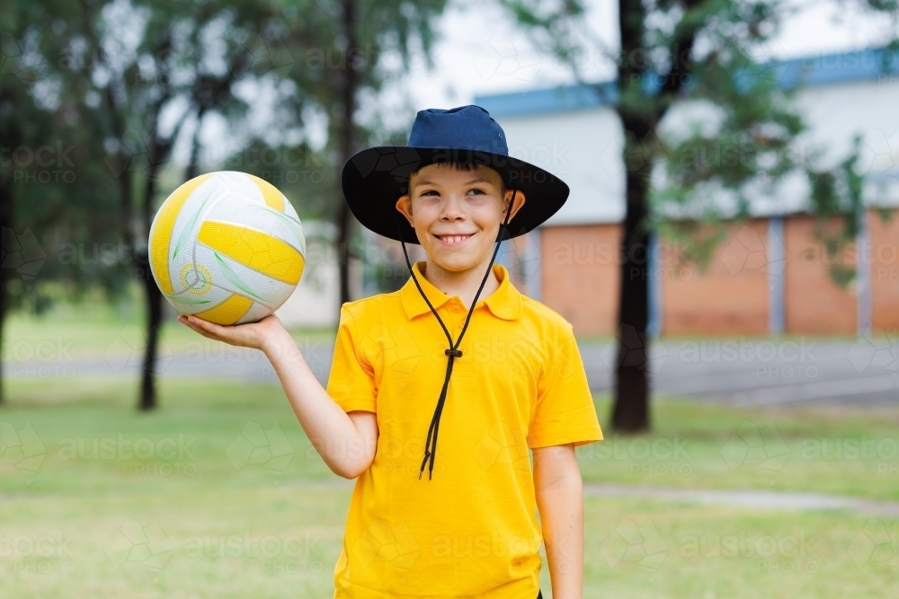 Happy Aussie school boy holding ball to play sports at school - Australian Stock Image