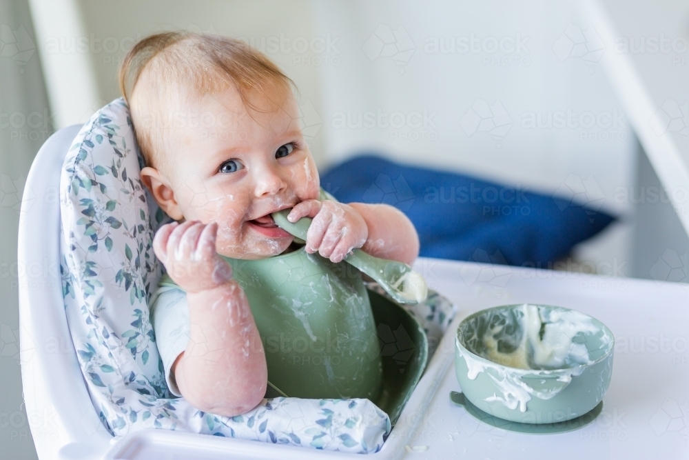 Happy australian baby in high chair eating yoghurt breakfast in high chair - Australian Stock Image