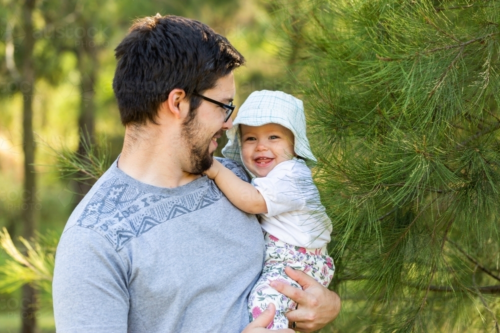 Happy baby and dad outside exploring nature and smiling beside casuarina tree - Australian Stock Image