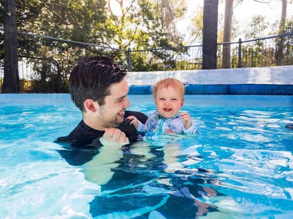happy baby and young dad playing in pool - excited fist pump - Australian Stock Image