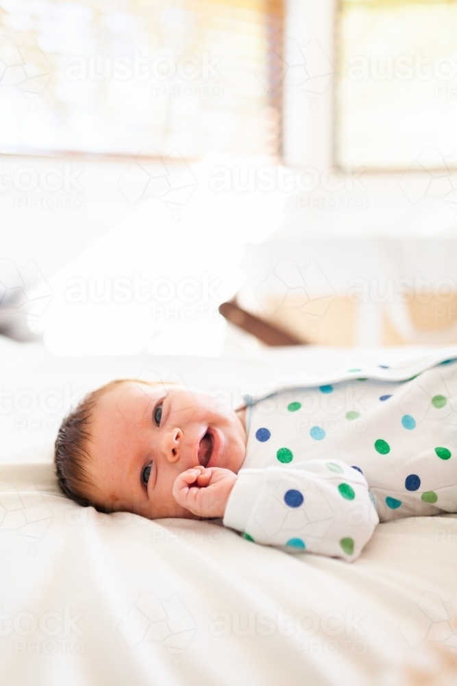 Happy baby child smiling lying on bed in parents room - Australian Stock Image