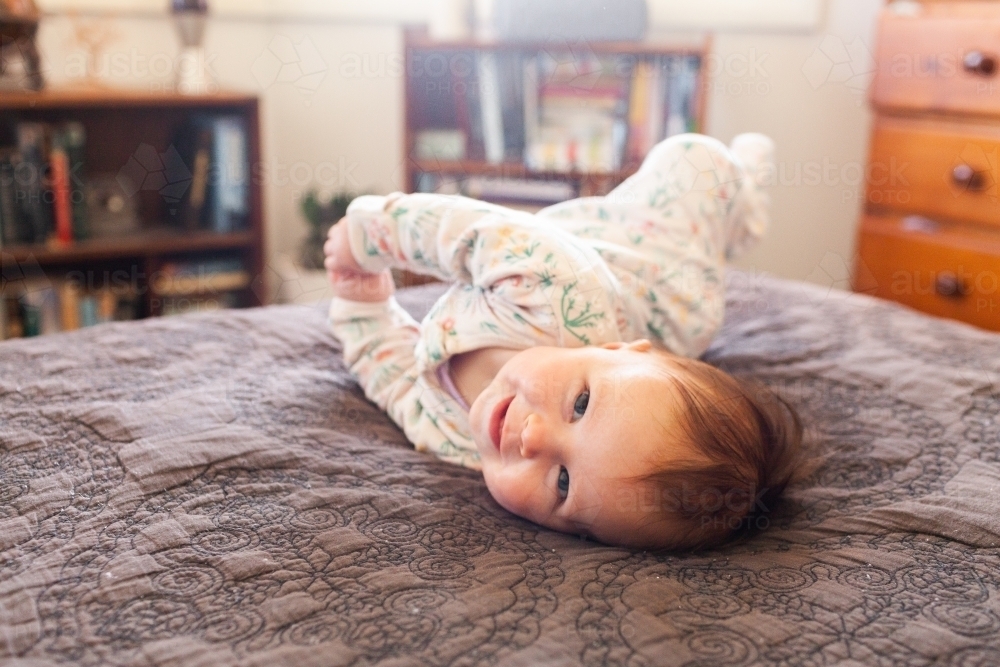 Image of Happy baby girl trying to roll over on parents bed in bedroom