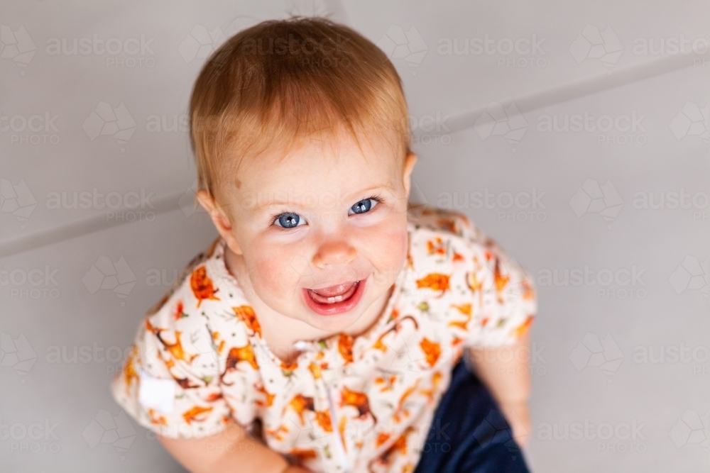 Happy baby grin with two teeth looking up at parent - Australian Stock Image