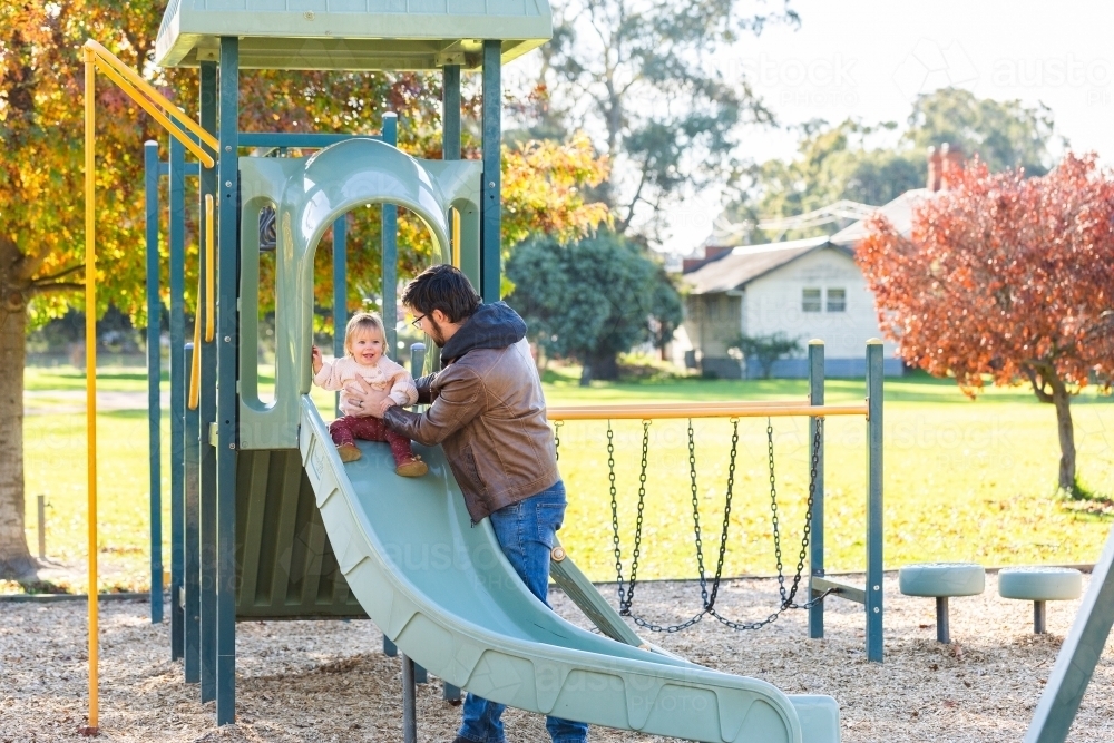 Image of Happy baby playing at park with father sliding down slippery ...