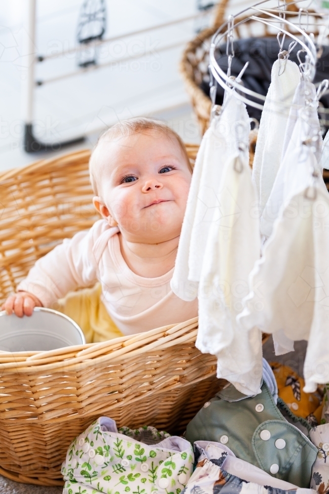 Happy baby sitting in washing basket with cloth nappies and re-usable wipes - Australian Stock Image