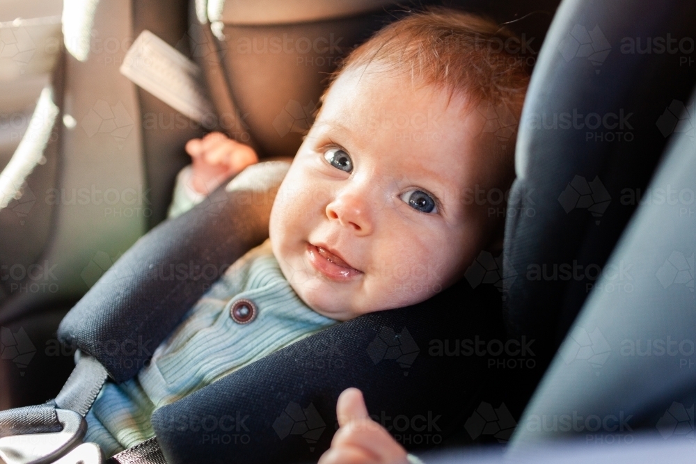 happy blue eyes baby clicked into rear facing child car seat - Australian Stock Image
