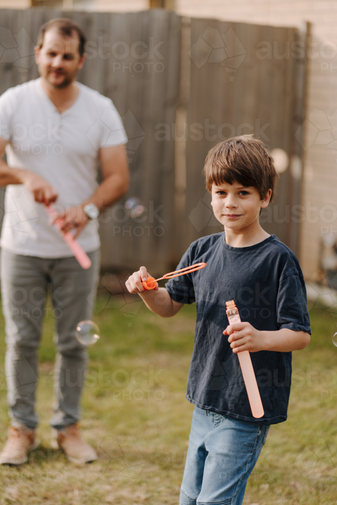 Happy boy blowing and playing with bubbles in backyard - Australian Stock Image