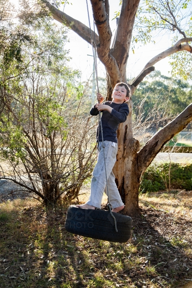 Happy boy on tyre swing in gum tree - Australian Stock Image