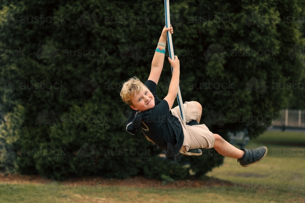 Happy boy playing on swing at playground - Australian Stock Image