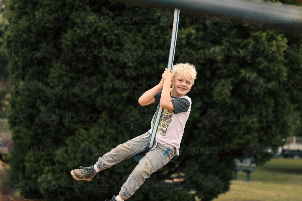 Happy boy playing on swing at playground - Australian Stock Image