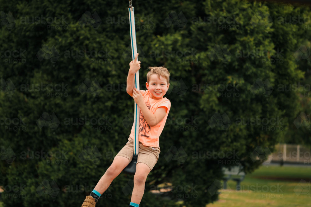 Happy boy playing on swing at the playground - Australian Stock Image