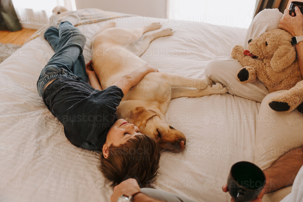 Happy boy snuggling in a cosy bedroom with his dog - Australian Stock Image