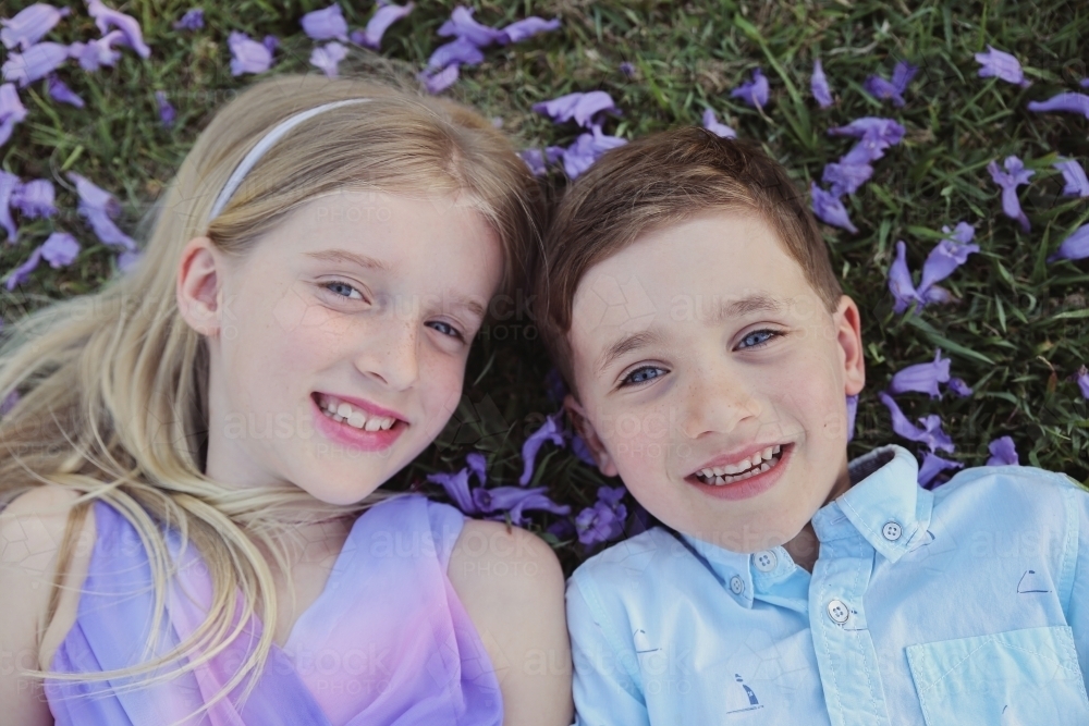 Happy brother and big sister lying on grass in the park - Australian Stock Image