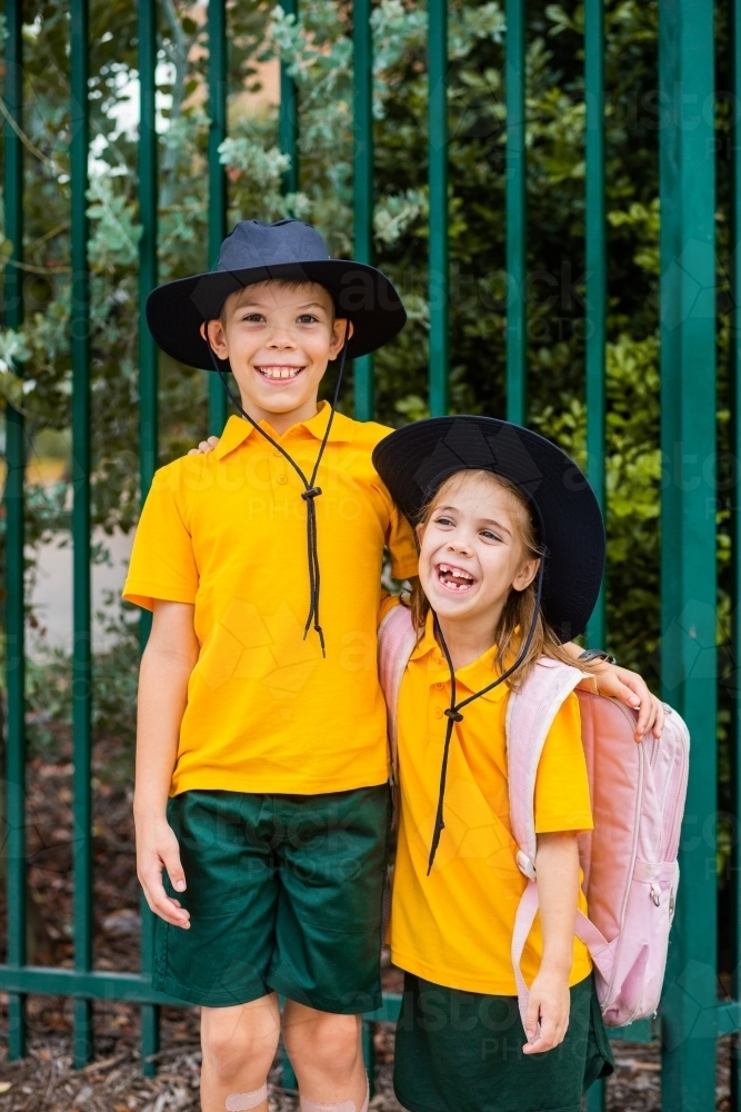 Happy brother and sister laugh and hug beside school fence outside - Australian Stock Image