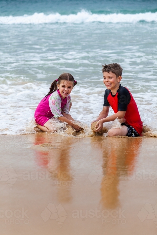 Happy brother and sister playing together on the beach - Australian Stock Image