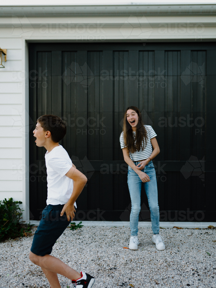 Happy brother and teen sister being silly together outside carport at home - Australian Stock Image