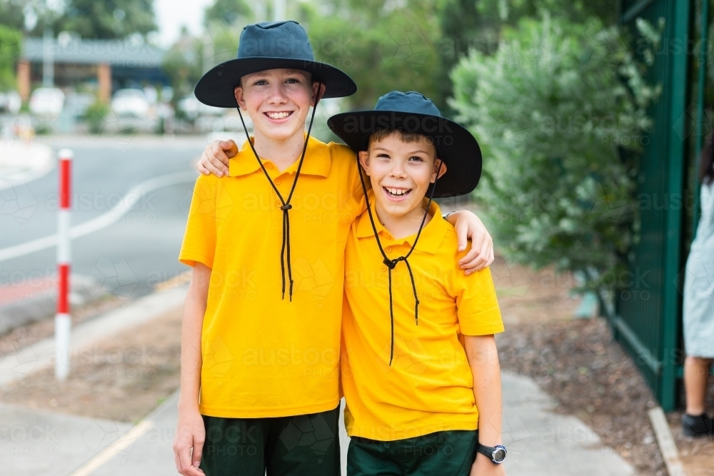 Happy brothers standing together before school wearing hats - Australian Stock Image