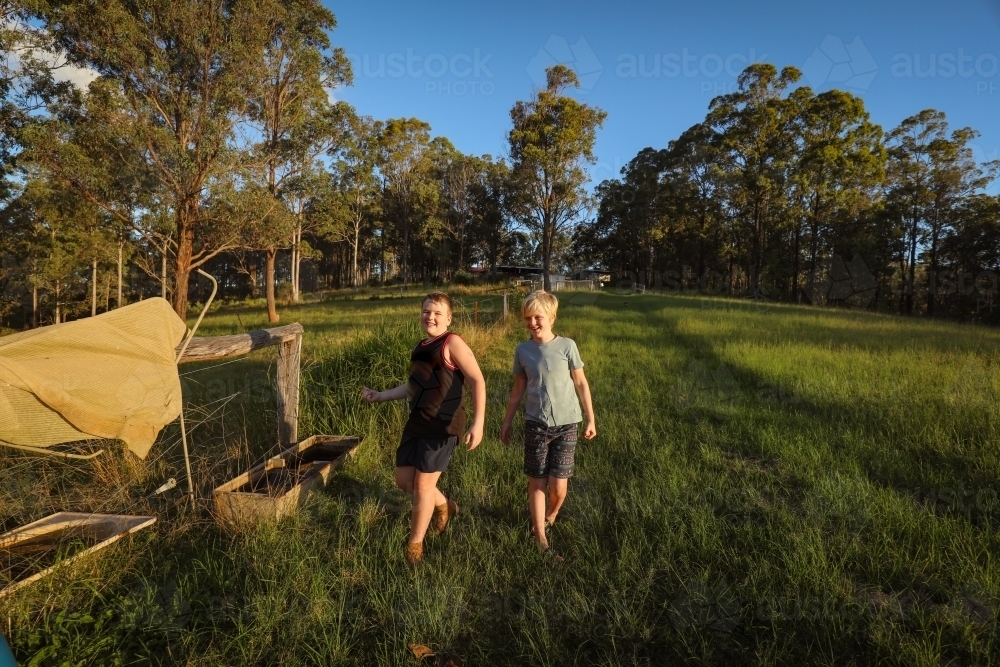 Happy brothers walking on farm in golden afternoon light - Australian Stock Image