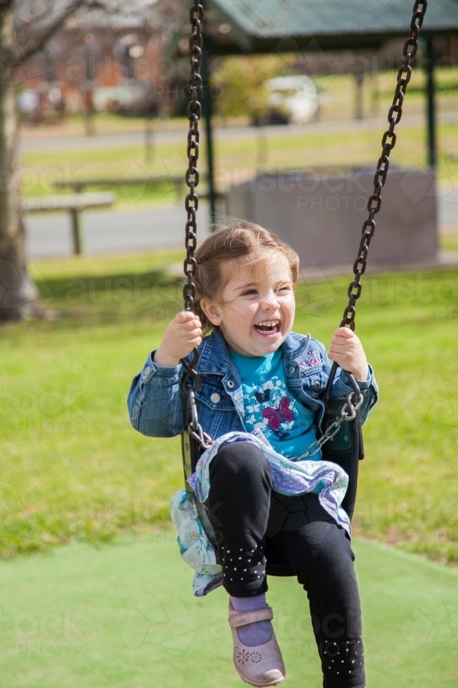 Happy child in swing at park - Australian Stock Image