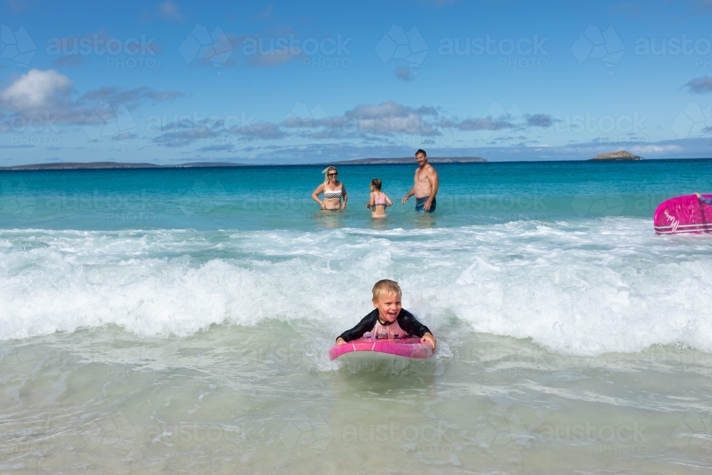 happy child lying on foam surfboard floating in on a wave - Australian Stock Image