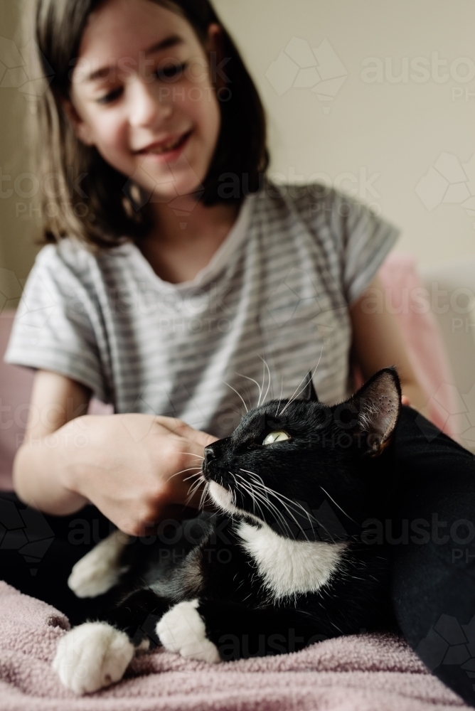 Happy child patting her pet cat in her bedroom. - Australian Stock Image