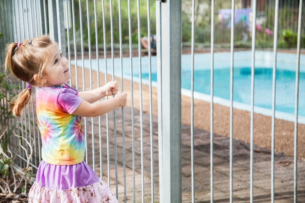 Happy child swinging off closed pool fence gate outside - Australian Stock Image