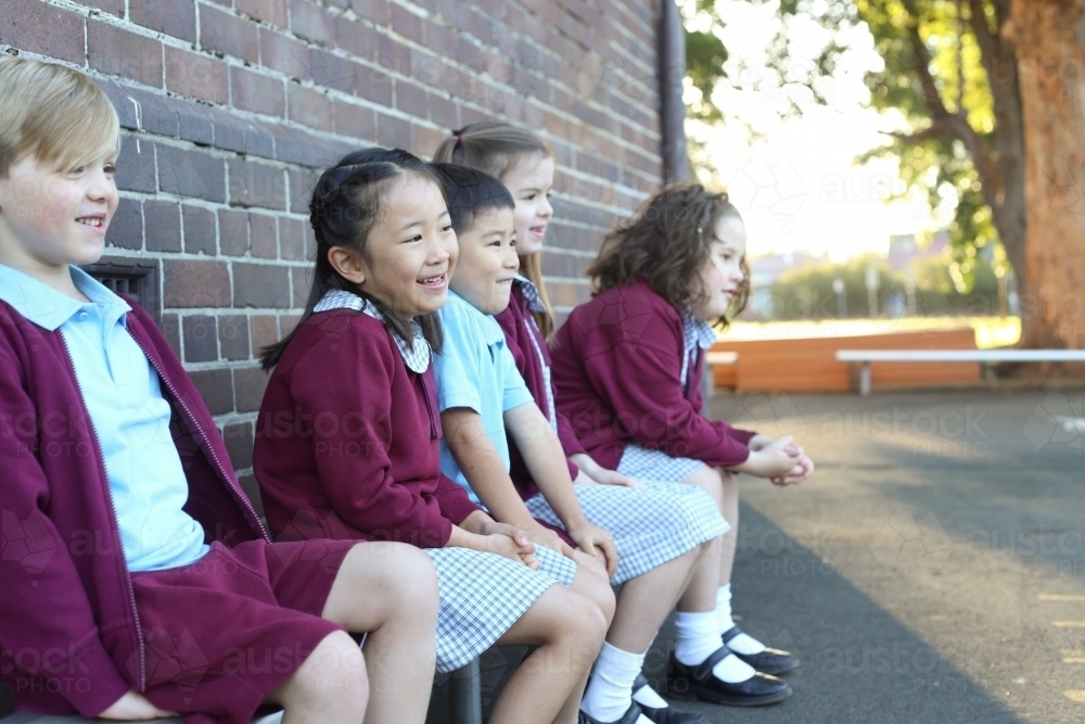Happy children sitting outside in the school playground - Australian Stock Image