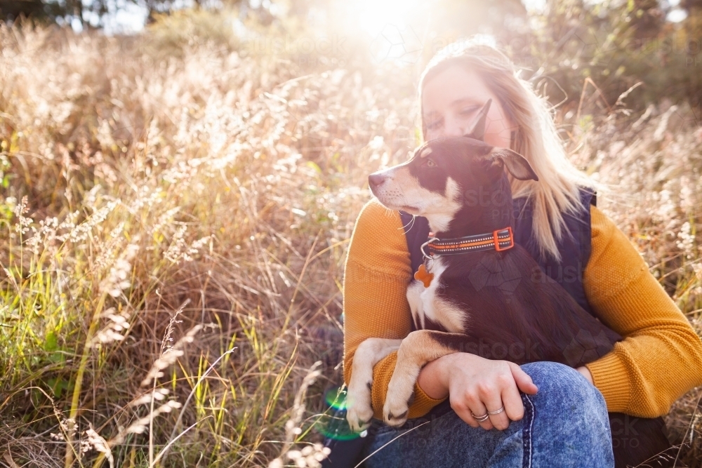 Happy country woman in her twenties with pet Australian Kelpie puppy dog in grass on farm - Australian Stock Image