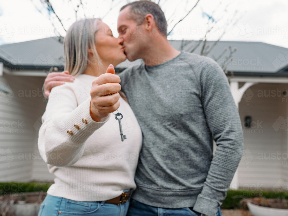 Happy couple kissing each other in the front yard holding a key of their new home - Australian Stock Image