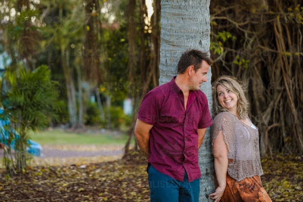 Happy couple leaning against palm tree at the park - Australian Stock Image