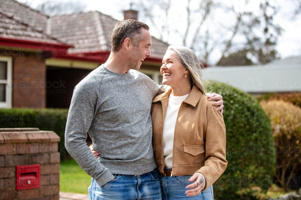 Happy couple standing arm-in-arm looking at each other in the front yard - Australian Stock Image