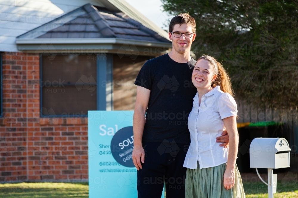 Happy couple standing infront of newly purchased house with sold sign - Australian Stock Image
