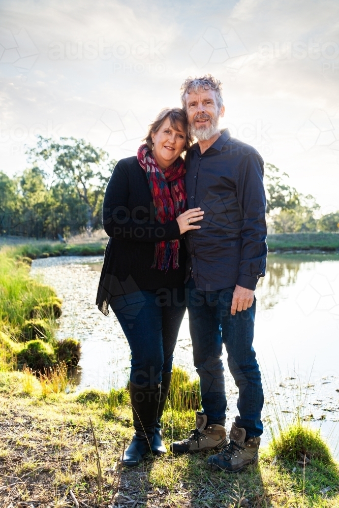 Happy couple standing together by dam in paddock - Australian Stock Image