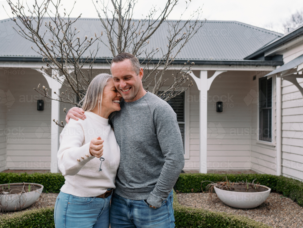 Happy couple stands in the front yard holding a key of their new home - Australian Stock Image