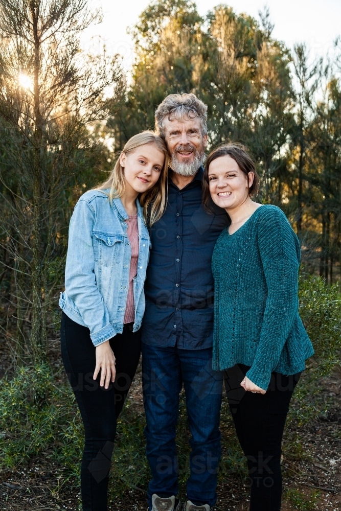 Happy dad with his two teenage daughters hug together outside - Australian Stock Image