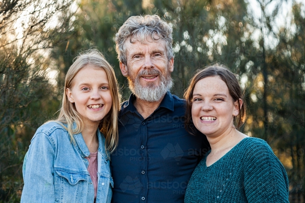 Happy dad with his two teenage daughters hug together outside - Australian Stock Image